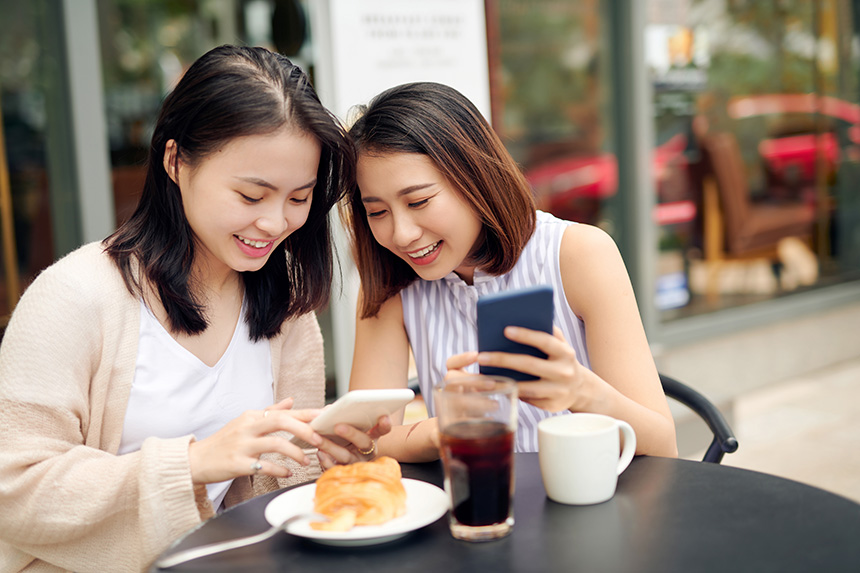 Two women using their phones while having coffee at a café.