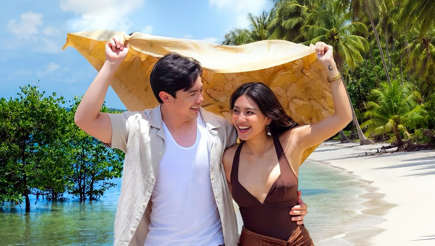 Kara (Nadine Lustre) and Jao (Alden Richards) smile as they hold up a shared sarong to block the sun.