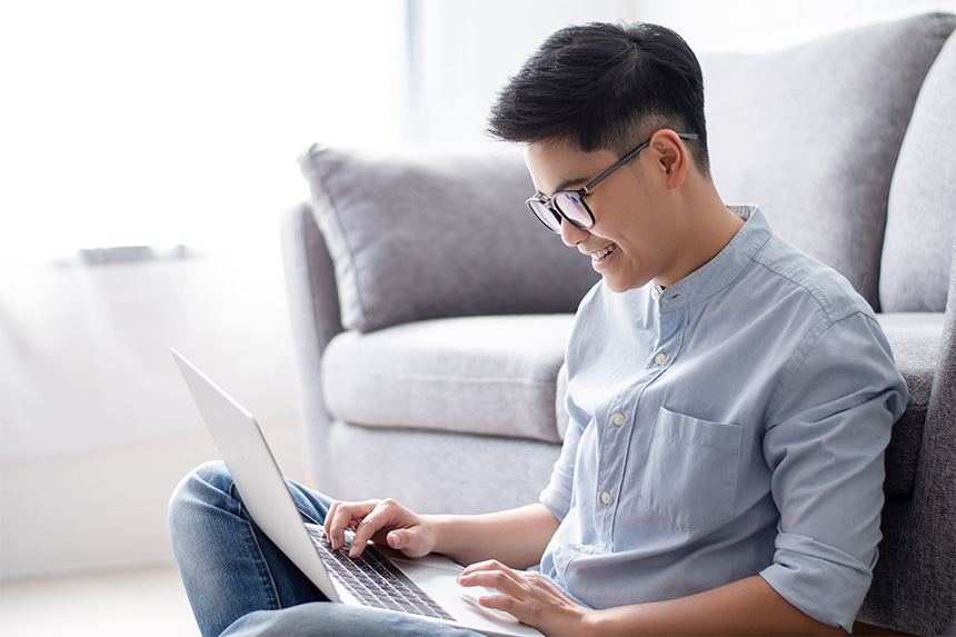 Man smiles while using his laptop to apply for documents and other visa requirements online.